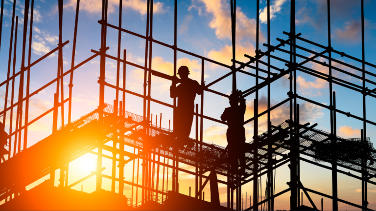 construction site scaffolding in silhouette with two people standing on it. Sun is low in the sky, a firey orange to suggest fire risks.